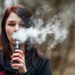 Vape teenager. Brunette girl smoking an electronic cigarette on the street in the spring.